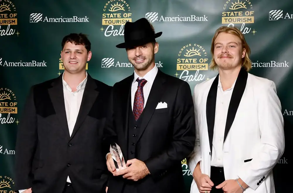 3 guys standing on a red carpet with awards